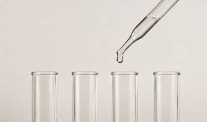 A dropper releasing a liquid sample above four test tubes